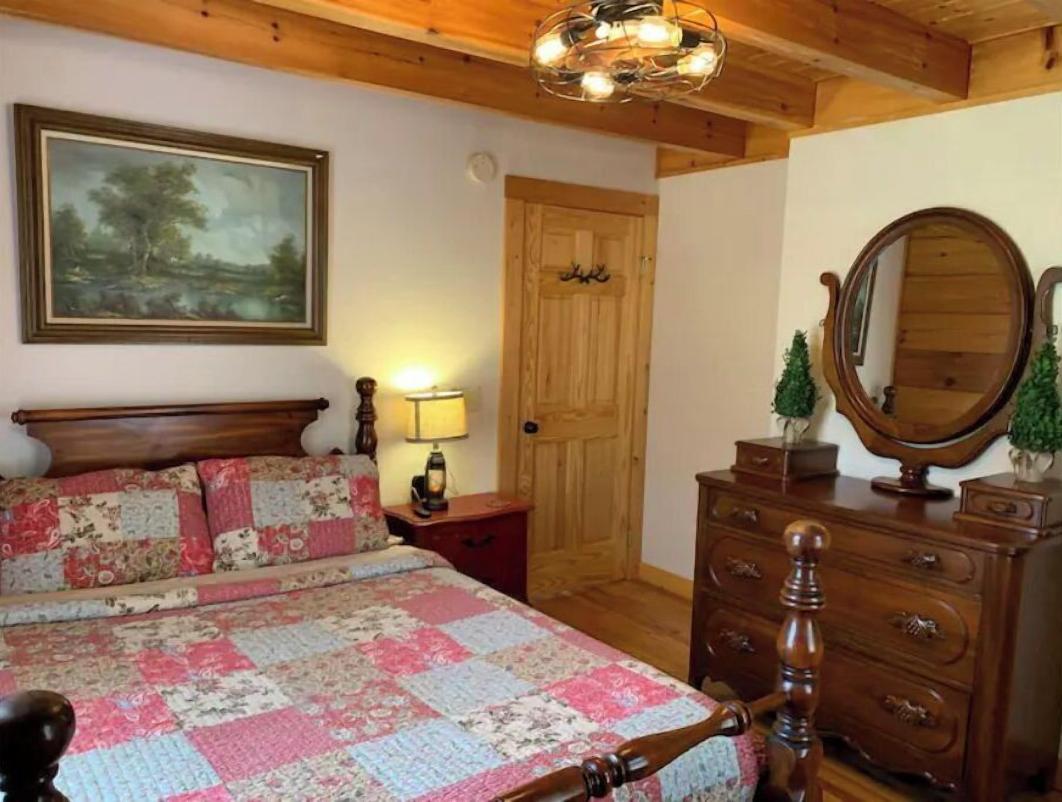A bedroom with a wooden bed, a quilt, a wooden dresser, a mirror, and a door.