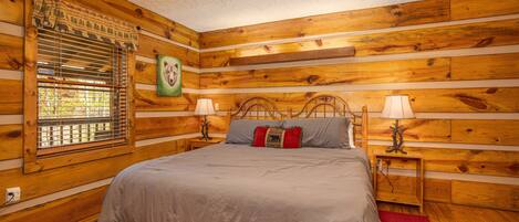 Um quarto estilo cabana de madeira com uma cama, duas mesas de cabeceira com abajures, uma janela com persianas e uma prateleira fixada na parede.