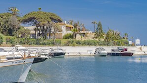 Un port de plaisance avec plusieurs bateaux amarrés, un mur de pierre et, au fond, un bâtiment avec un toit jaune.