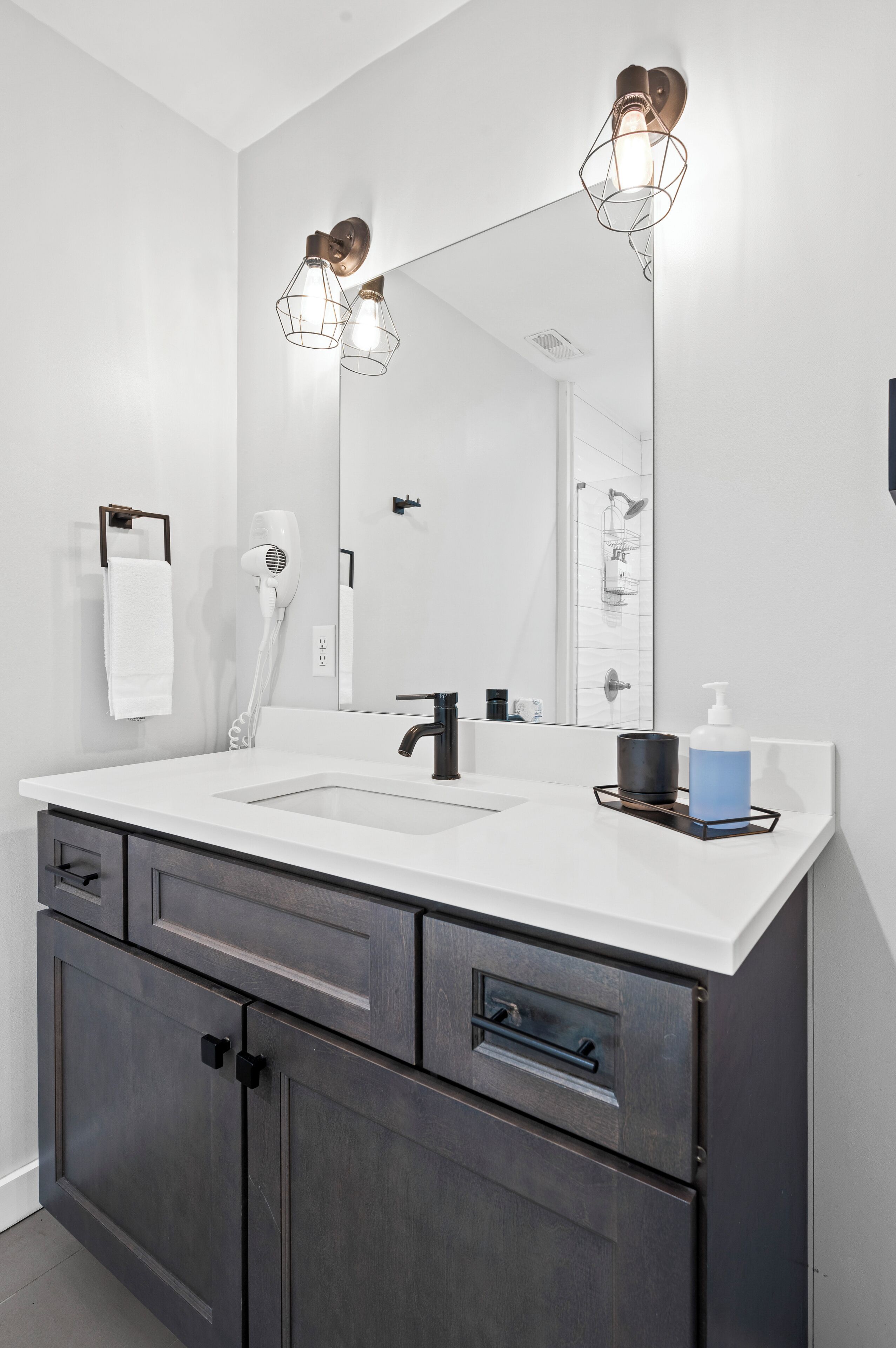 Un baño moderno con tocador blanco, armarios oscuros, un espejo grande y dos luces empotradas.