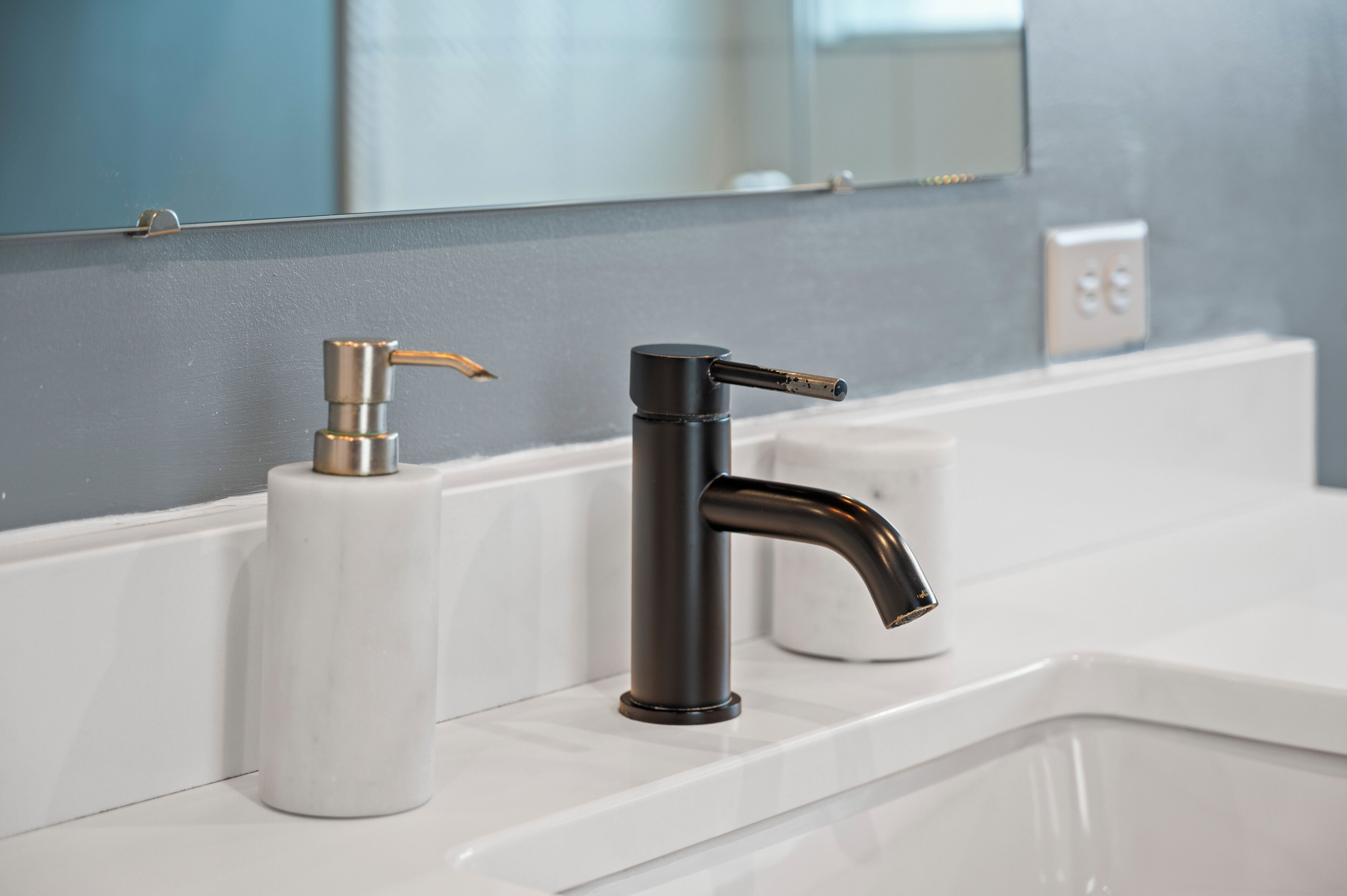 Un baño con un lavamanos blanco, un grifo negro y un dispensador de jabón blanco.