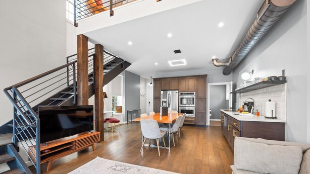 A spacious living area with a wooden staircase, a dining table with chairs, a kitchen with modern appliances, and a large TV. - Baldwin Flats (Covington)
