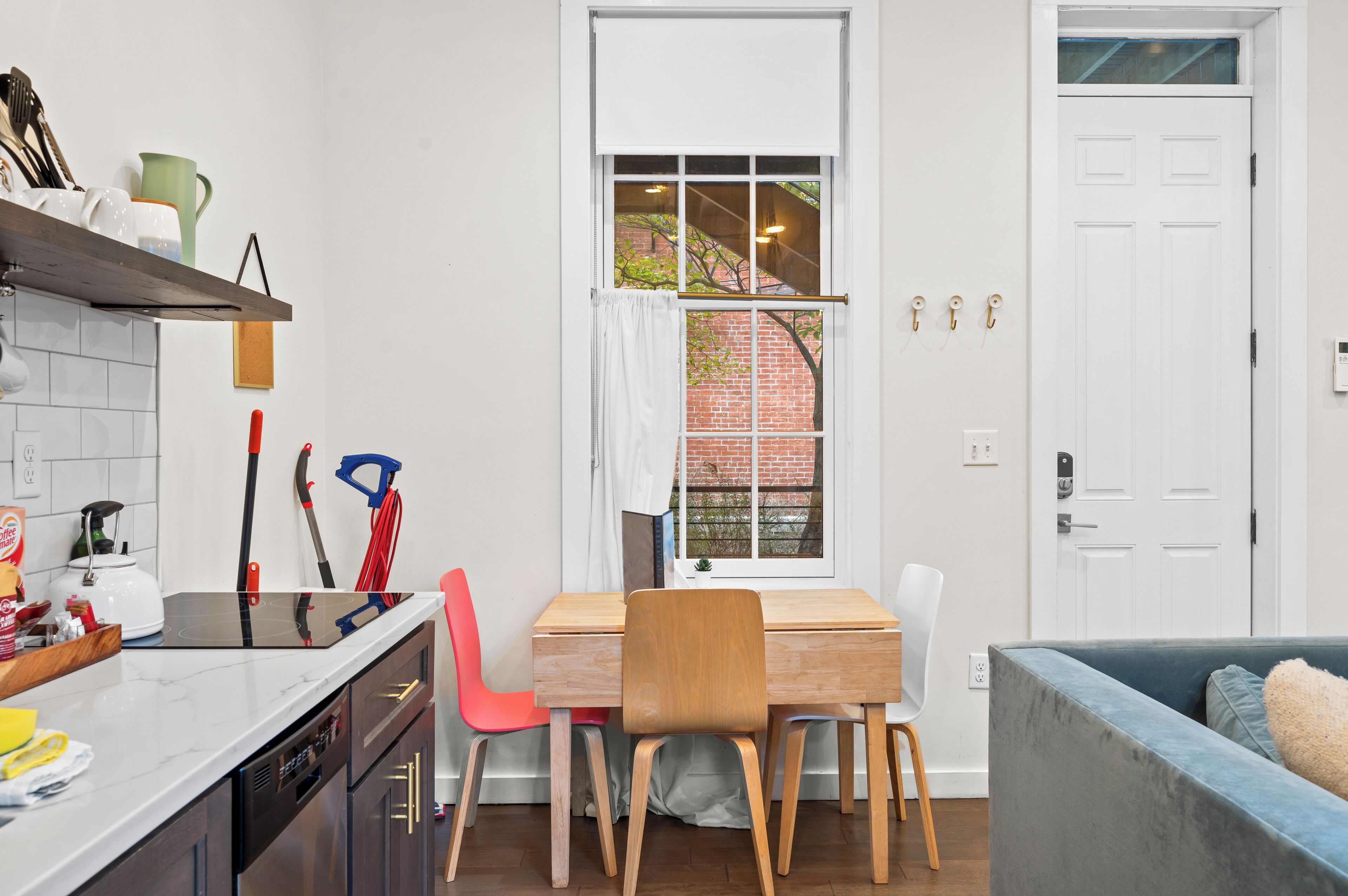 A compact kitchen with a dining area, a window with a view of a brick building, and a white door.
