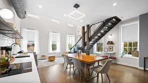 A modern kitchen with a built-in oven, a dining area with a wooden table and chairs, and a staircase leading to an upper level. - Baldwin Flats (Covington)