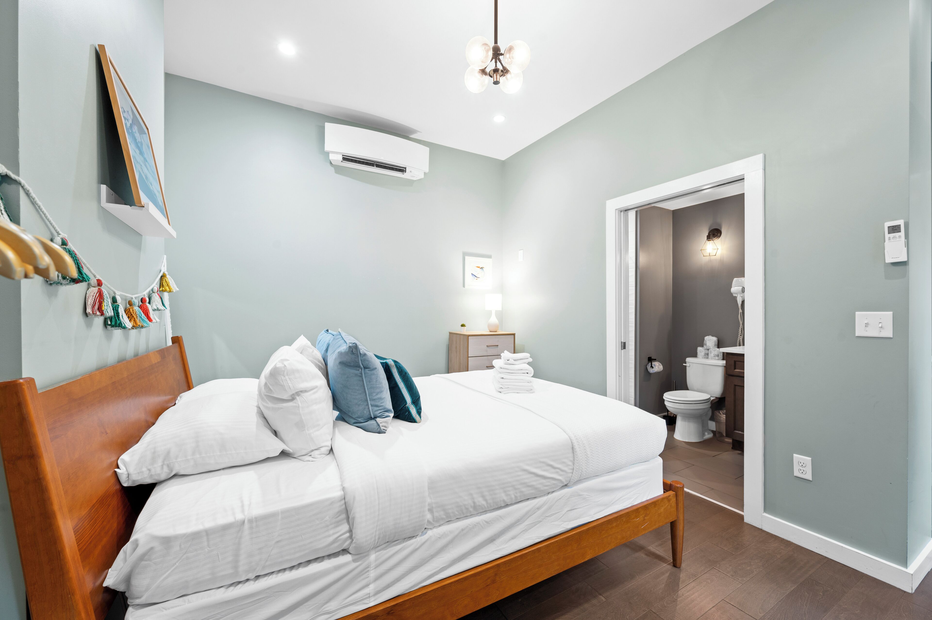 Una cama bien hecha con sábanas blancas y un cabecero de madera, una mesita de noche con una lámpara y un aire acondicionado instalado en la pared.
