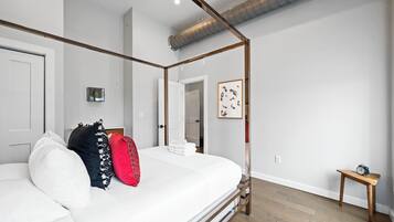 A modern bedroom with a four-poster bed, a small bedside table, and a framed artwork on the wall.