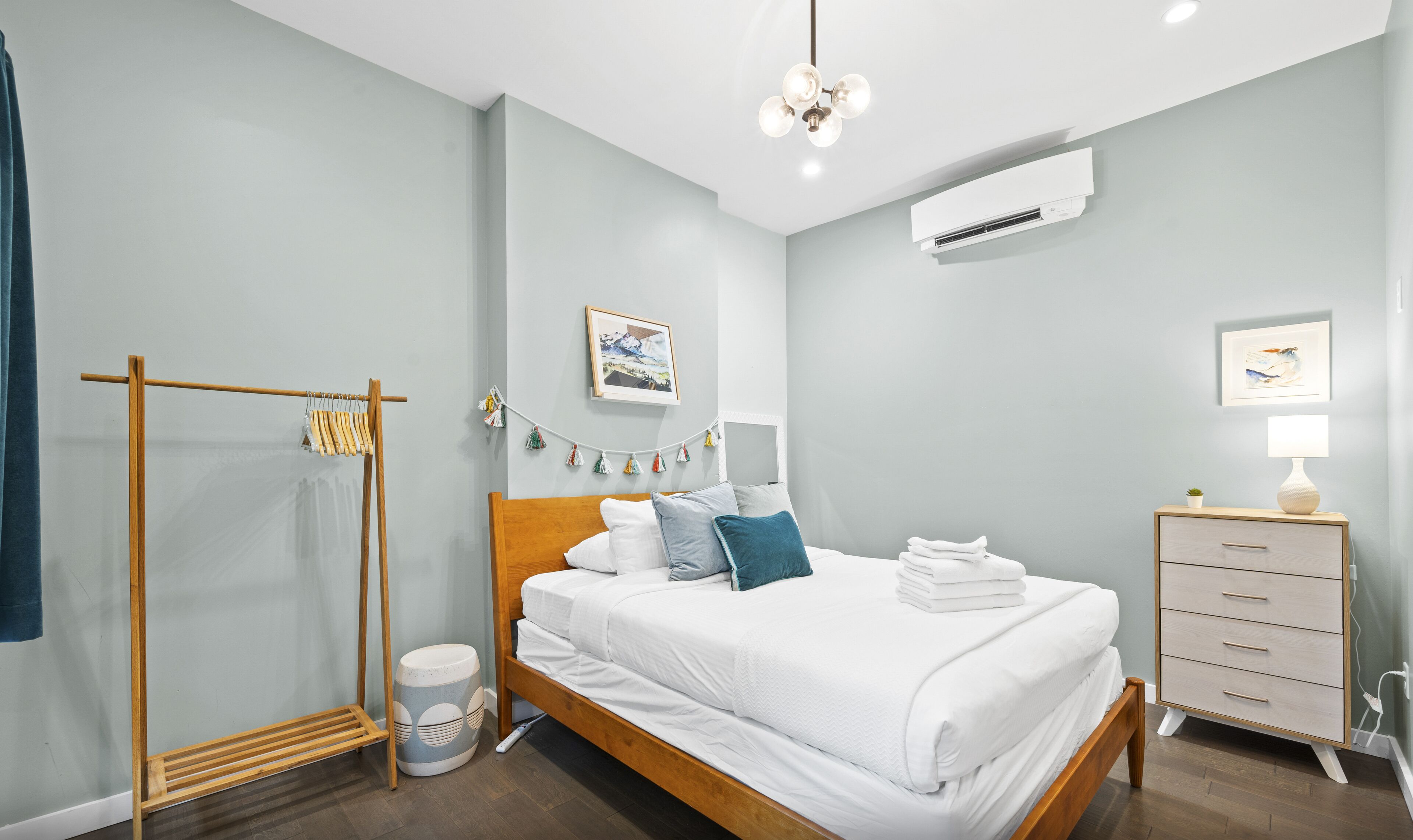 A bedroom with a bed, a wardrobe, a hanging light fixture, an air conditioning unit, and a small plant.