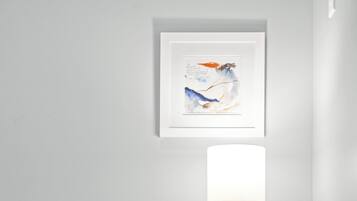 Una stanza dal design minimalista con un armadietto in legno, una piccola pianta in vaso, una lampada bianca e un'opera d'arte incorniciata appesa al muro.