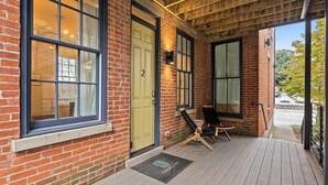 A brick building with large windows, a wooden deck, and a door with the number 2. - Baldwin Flats (Covington)