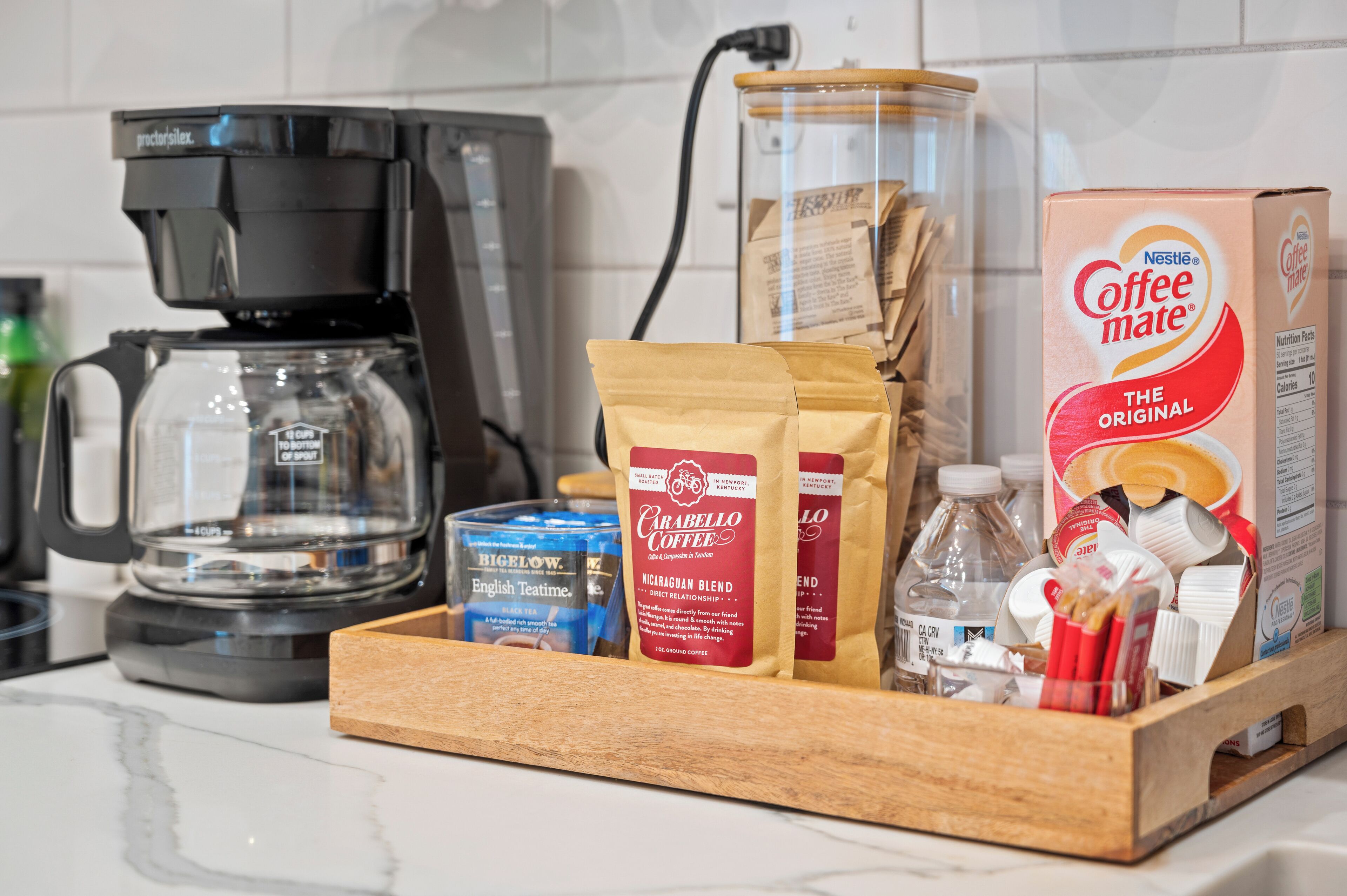 A kitchen counter with a coffee maker, a coffee bean grinder, a coffee maker box, and a coffee mug.