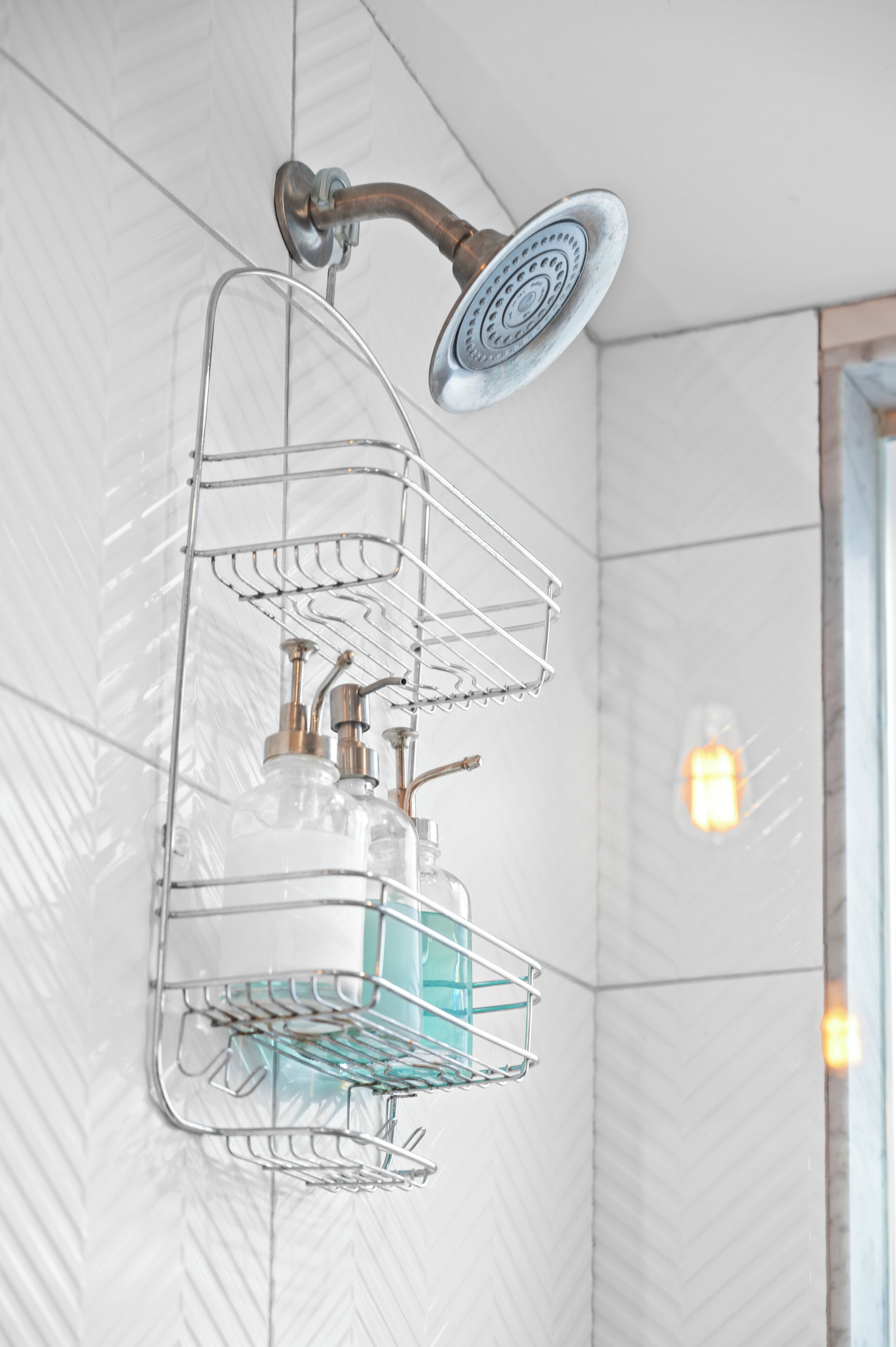 A bathroom with a shower head, a metal rack with bottles, and a light fixture on the wall.