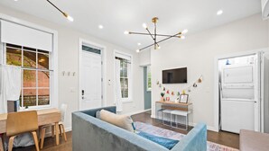 A modern living room with a sofa, a dining area, and a kitchen. - Baldwin Flats (Covington)