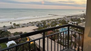 A balcony with a view of a beach and ocean during sunset.