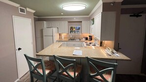 A compact kitchen with a central island, white cabinetry, and a small dining area with two chairs.