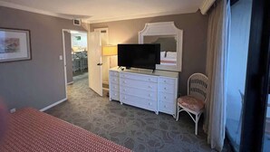 A hotel room with a bed, a dresser with a TV, a chair, and a door leading to a bathroom.