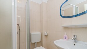 Casa de banho com sanita, chuveiro, lavatório e espelho com moldura azul.