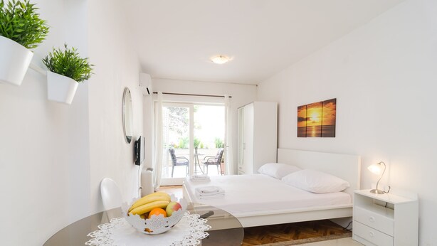 Quarto moderno com mesa de vidro, uma tigela de frutas, cama, mesa de cabeceira e vista para o exterior.