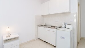Cozinha compacta com armários brancos, pia, fogão, chaleira e torradeira.