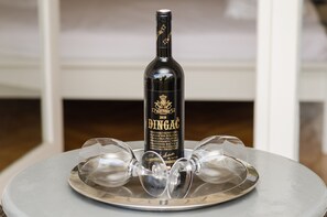 Une bouteille de vin DINGAC, avec son étiquette, est posée sur une table ronde, à côté de deux verres à vin vides.