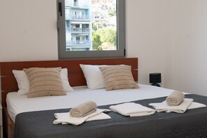 Habitación de hotel con cama, almohadas, ventana y mesita de noche.