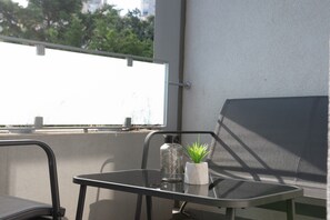 A balcony with a table, a chair, a potted plant, and a glass bottle.
