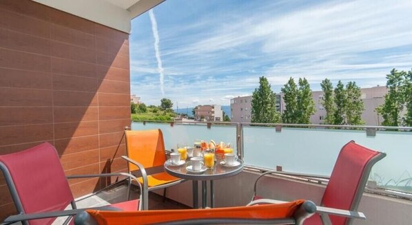 A balcony with a table set for breakfast, chairs, and a view of buildings and trees.