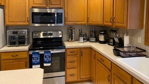 Una cocina con armarios de madera, un microondas de acero inoxidable, una estufa y varios electrodomésticos.