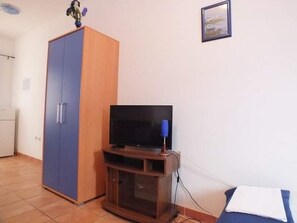 A small room with a wooden wardrobe, a television on a wooden stand, and a bed with a white pillow. - Villa Sarajevo - Studio Apartment with Terrace (Vodice)