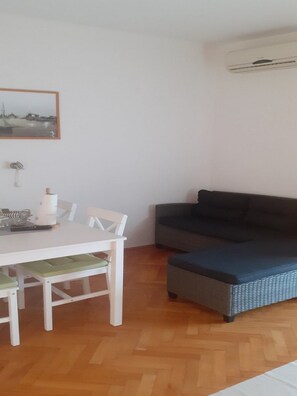 A room with a dining table, chairs, a grey sofa, a white wall with a framed picture, and an air conditioning unit. - Apartments Biserka - Two Bedroom Apartment with Terrace and Sea View (Rab)