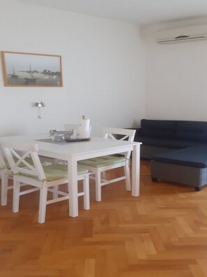 A dining area with a white table and chairs, a blue sofa, and a wooden floor. - Apartments Biserka - Two Bedroom Apartment with Terrace and Sea View (Rab)