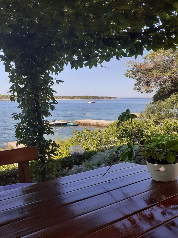 A wooden table with a potted plant, a bench, and a view of a calm sea with boats.
