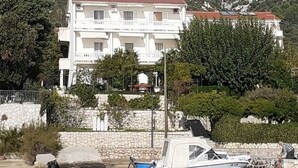 A multi-story building with balconies, surrounded by greenery and mountains. - Apartments Biserka - One Bedroom Apartment with Balcony and Sea View (Rab)