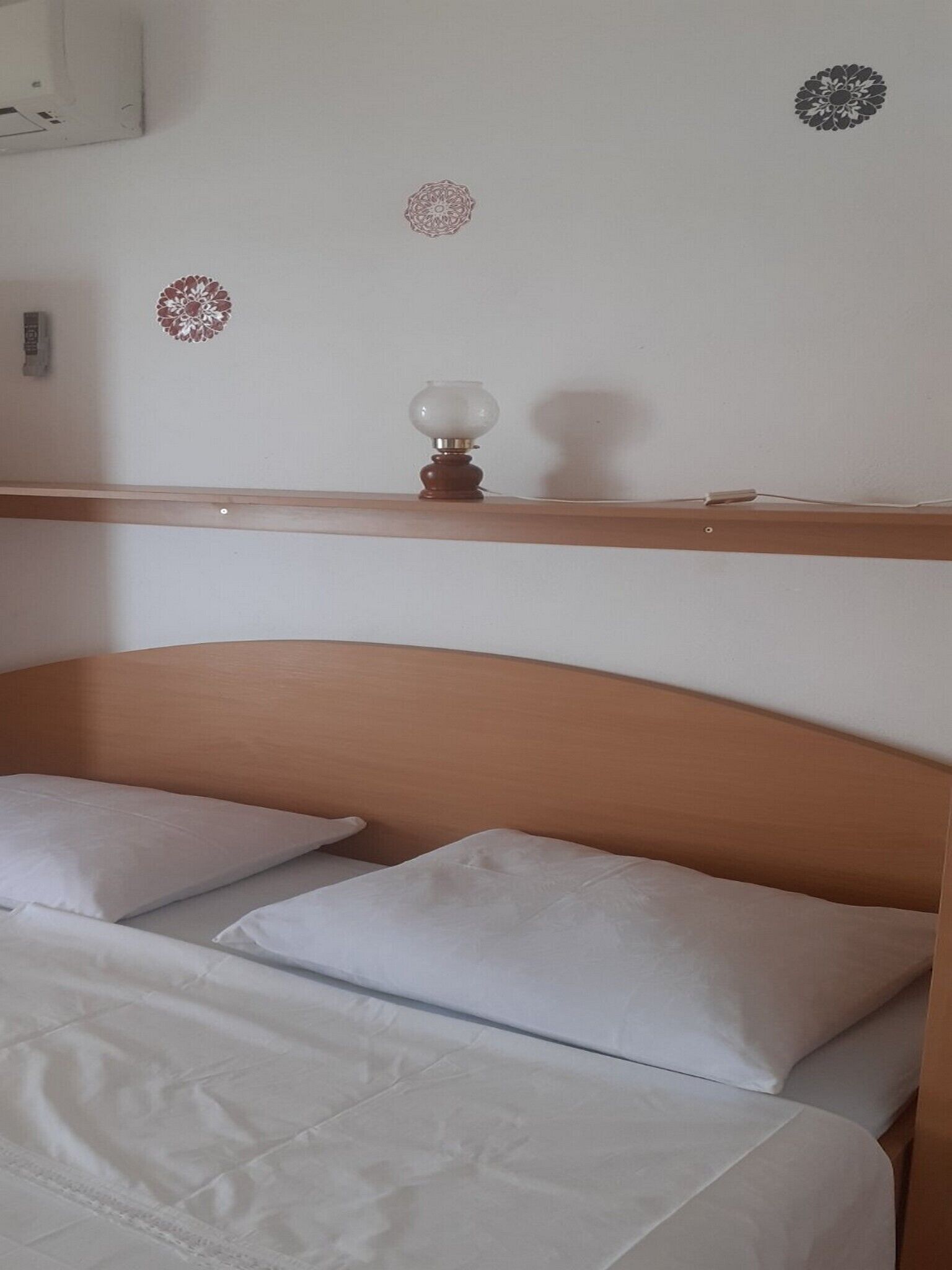 A hotel room with a wooden headboard, two white pillows, and a bedside table with a lamp.