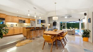 A modern kitchen with wooden cabinets, a central island with bar stools, and a dining area with yellow chairs. - Lush & Tranquil 3BR Palm Springs Oasis Pool & Spa (Palm Springs)