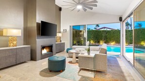 A modern living room with a fireplace, a flat-screen TV, and a pool view. - Lush & Tranquil 3BR Palm Springs Oasis Pool & Spa (Palm Springs)