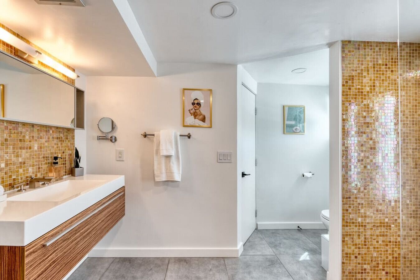 A modern bathroom with a large mirror, a wooden vanity, and a shower area with mosaic tiles.