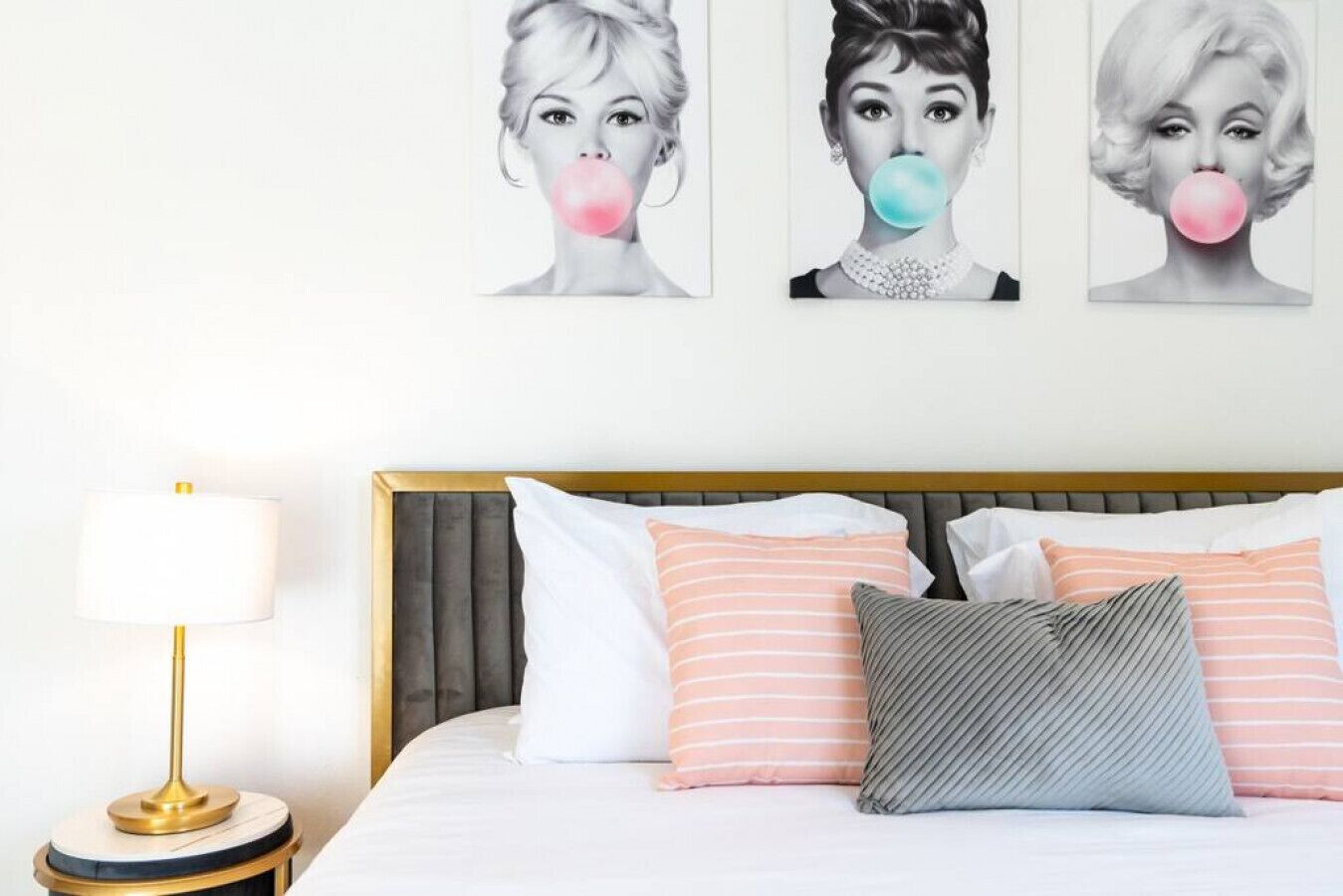 A hotel room with a bed, pillows, a nightstand, and a wall with three framed pictures.