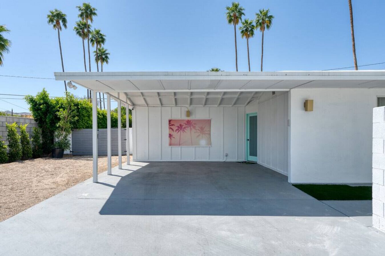 A covered outdoor area with a concrete floor, a green door, and a wall-mounted painting.