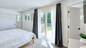Ein Schlafzimmer mit einem Bett, einem Fenster mit Vorhängen und Blick auf einen Garten.