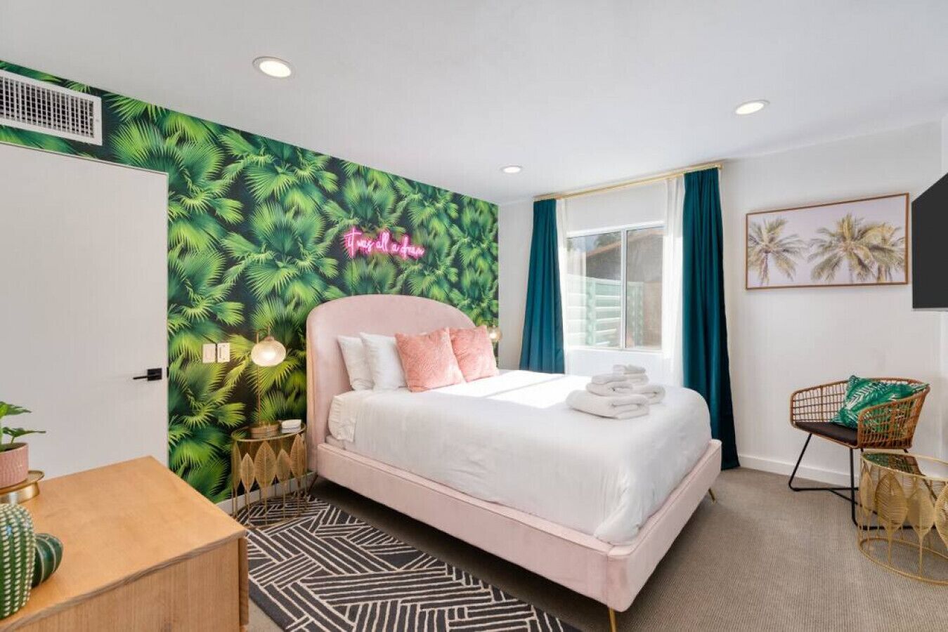 Een moderne slaapkamer met een bed, een neonbord, een raam met gordijnen en een muur met een tropisch bladmotief.