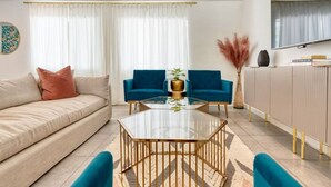 Ein modernes Wohnzimmer mit einem beigefarbenen Sofa, einem Glastisch und zwei blauen Sesseln.
