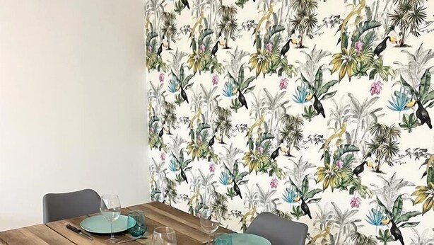 Une table à manger avec de l’argenterie et des verres de couleur turquoise, placée devant un papier peint à motifs floraux.