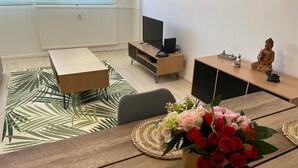 Un salon moderne avec une table à manger en bois, un téléviseur posé sur un meuble, une statue et une figurine de Bouddha.