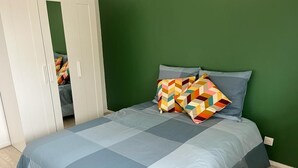 Une chambre à coucher avec un lit, des murs verts et une armoire blanche.