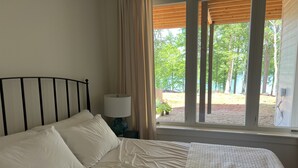 Un letto con biancheria bianca, un comodino con una lampada e una finestra con tende.