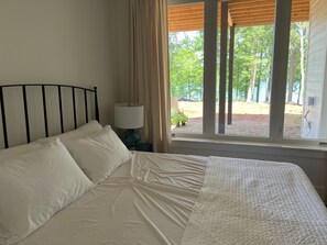 Un lit avec une literie blanche, une table de chevet avec une lampe et une fenêtre avec des rideaux.