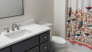 Un bagno con un lavandino bianco, mobili scuri, un water e una tenda da doccia con motivo floreale.