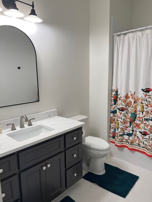 Une salle de bain avec un lavabo blanc, des meubles sombres, des toilettes et un rideau de douche orné d’un motif d’oiseaux.