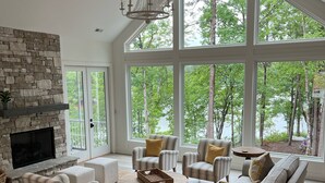 A spacious living room with a stone fireplace, large windows, and a high ceiling. - Carolina’s Cottage Cove-Lake Keowee (Seneca)