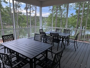 Une terrasse extérieure couverte, dotée d’une table et de chaises, entourée d’une balustrade blanche et offrant une vue sur une zone boisée.